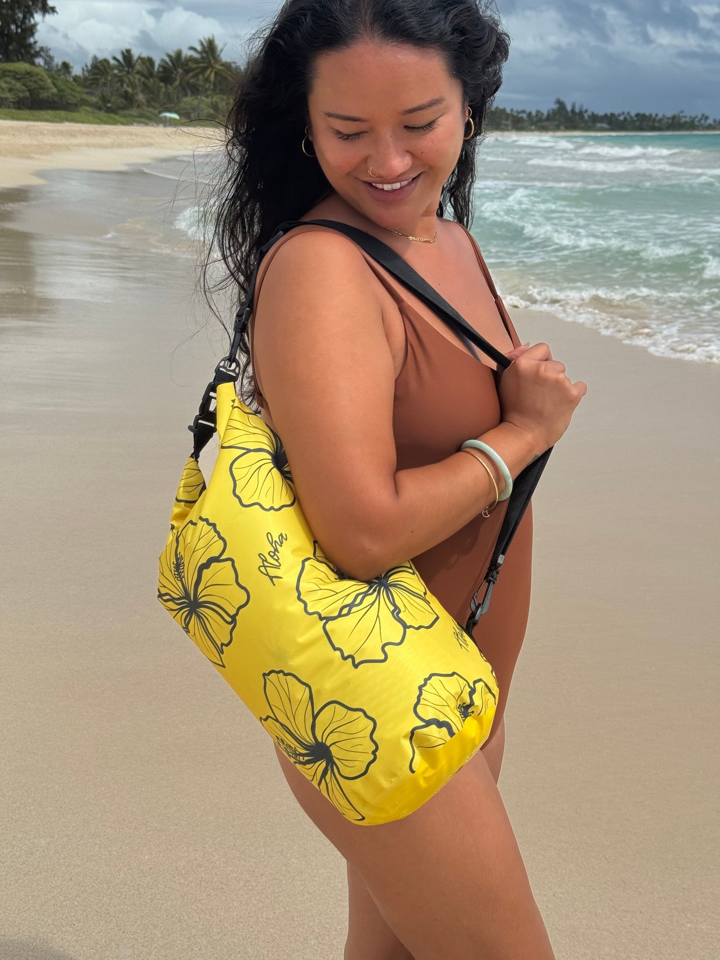 Woman in a swimsuit with a yellow floral dry bag on her shoulder.