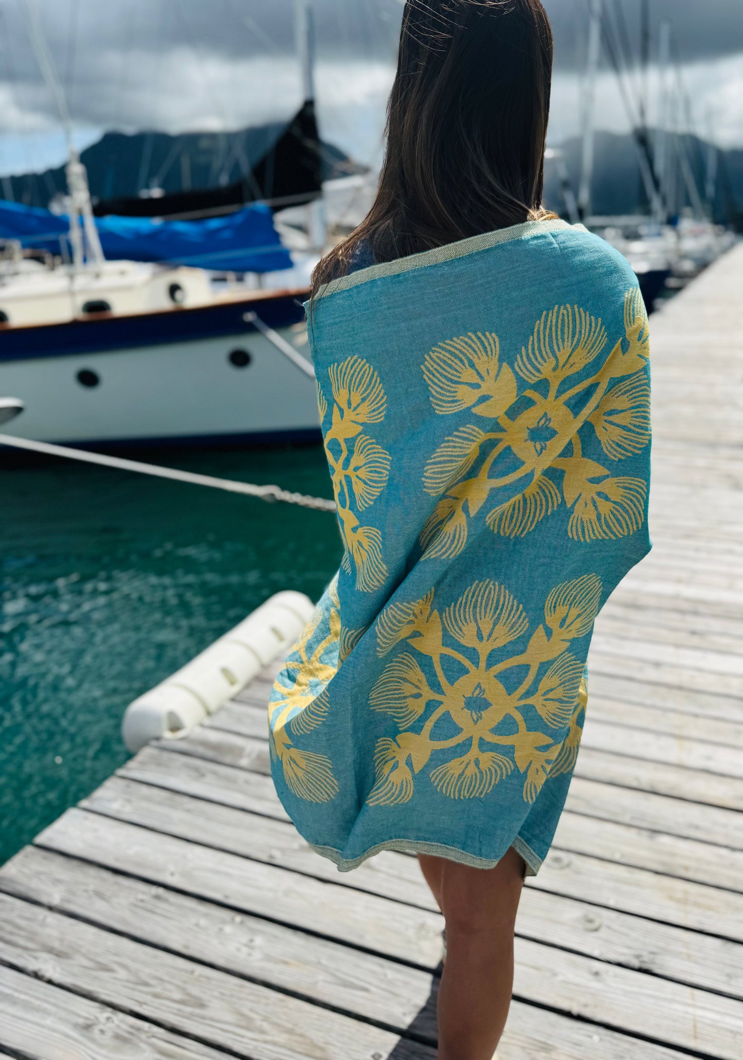 Woman with a tel and yellow towel wrapped around her walking along a dock.
